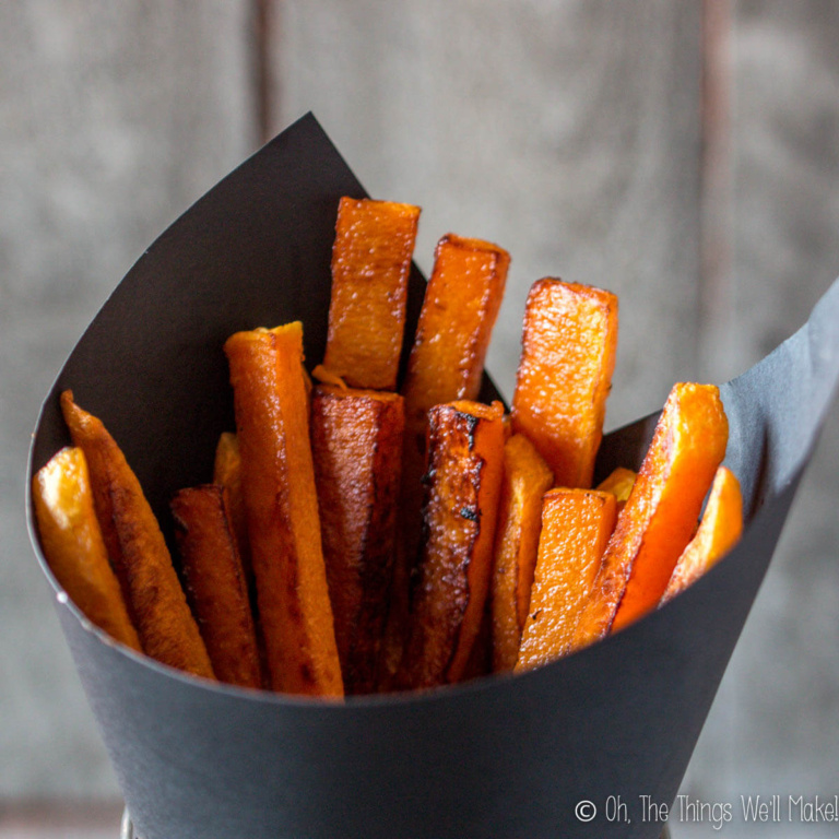 A black paper cone brimming with golden-brown pumpkin fries.