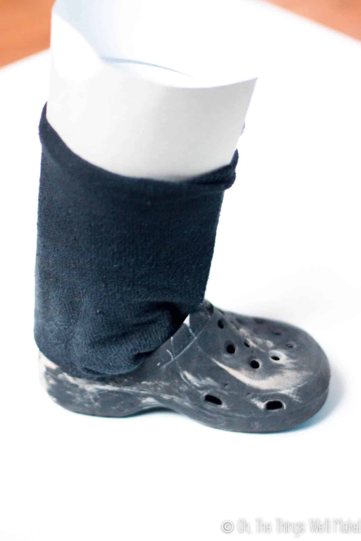 Crocs type shoes with a large sock inside of them which is held up by a cylinder of cardboard in the position of a leg/foot.
