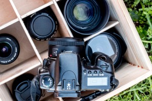 A camera sitting on top of a wooden box filled with different objective lenses
