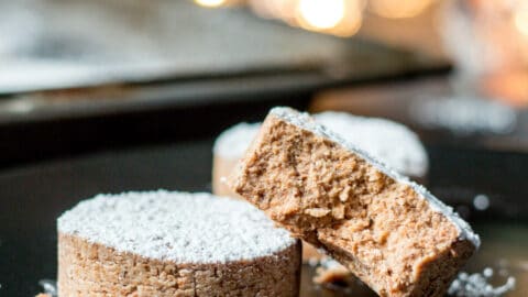 Two homemade mantecados or polvoron cookies on a plate with one broken open to reveal the smooth texture inside.