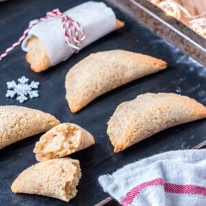 Homemade pastissets, a dessert empanadilla filled with a sweet boniato filling, on a baking tray with one broken open to show the filling.