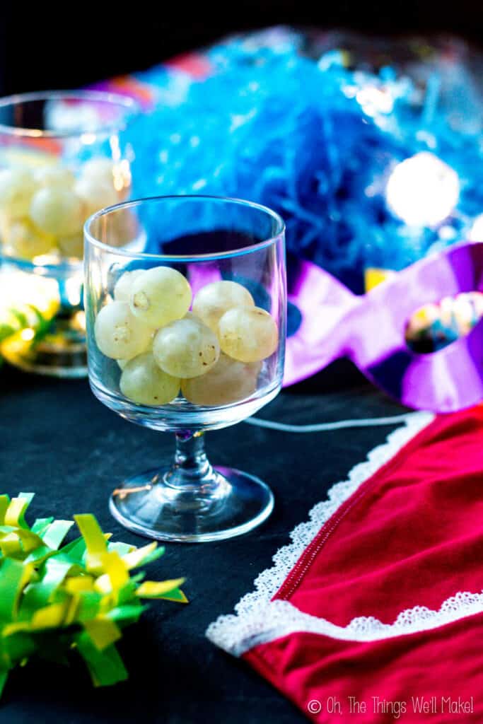 a glass filled with 12 lucky grapes next to red underwear, a mask, and other cotillion party favors.