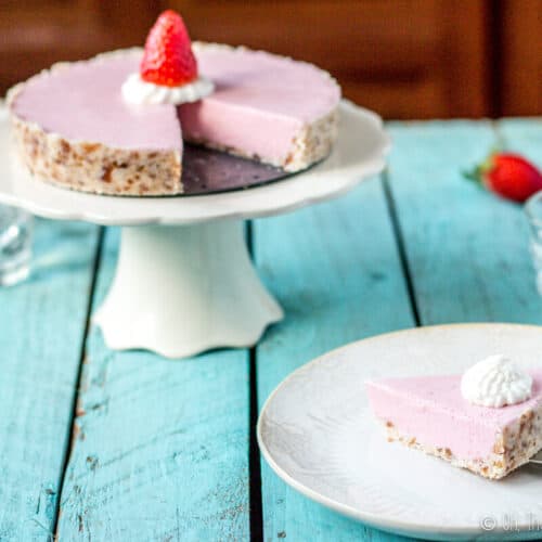 A paleo strawberrry cream pie on a cake stand with a slice missing. The slice is being places on a light beige plate with a spatula.