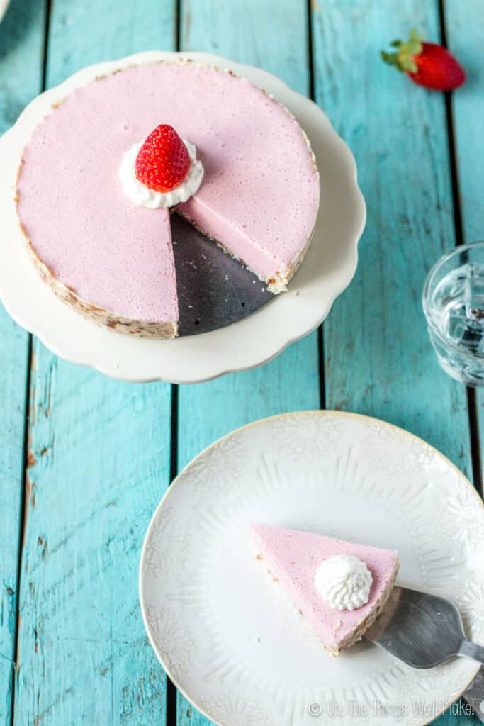 Overhead view of a no-bake strawberry cream pie from which a slice has been removed and is being placed on a beige plate with a spatula.