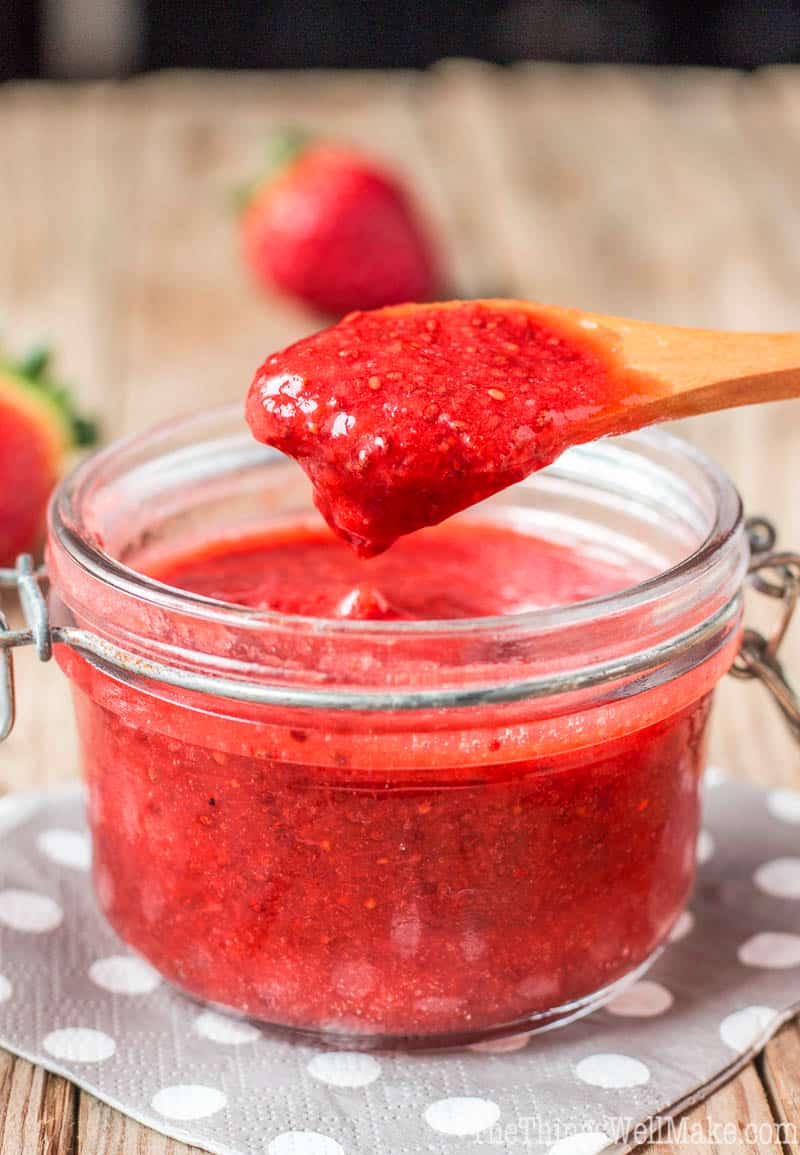 Closeup view of strawberry chia seed jam in a jar being scooped up by a wooden spoon