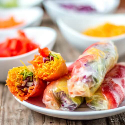 A plate full of spring rolls filled with colorful vegetables. One has been cut in half to show the filling.