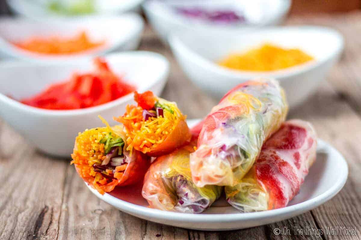 A plate full of spring rolls filled with colorful vegetables. One has been cut in half to show the filling.