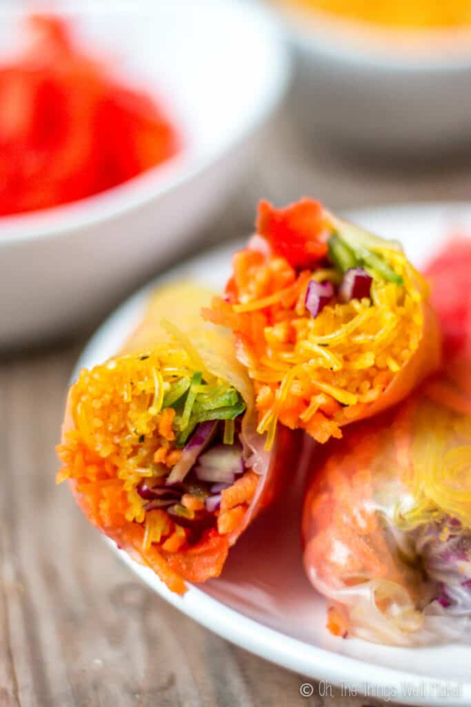 Closeup of a spring roll that has beeb cut in half on a plate showing the colorful rainbow of vegetables inside.