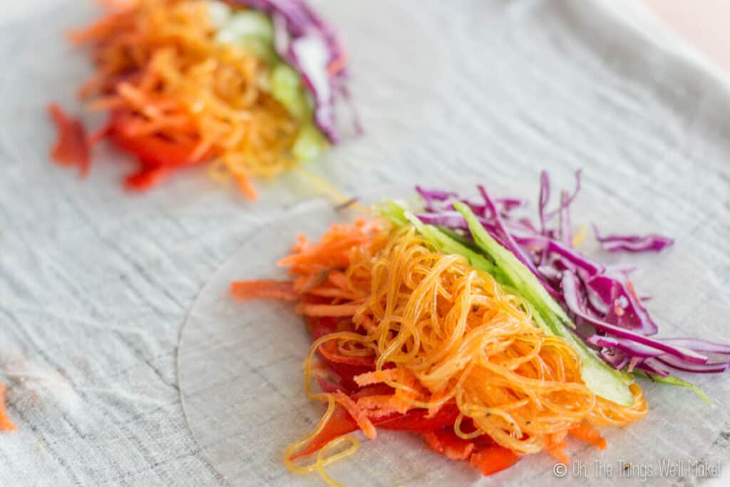 Overhead view of 2 spring rolls wrappers covered with colorful veggies and bean vermicelli, ready for rolling into spring rolls.