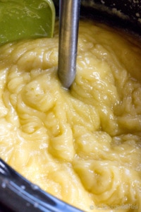 A closeup of a thick soap paste in a slow cooker with an immersion blender in it.