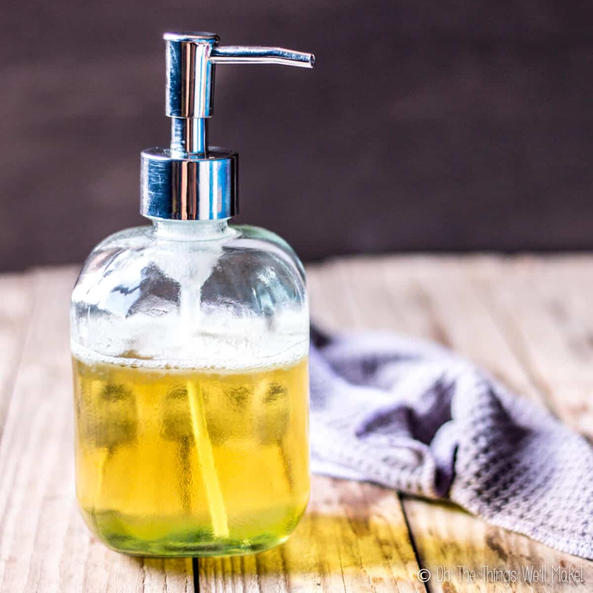 A bottle of homemade liquid Castile soap in a soap dispenser next to a washcloth.