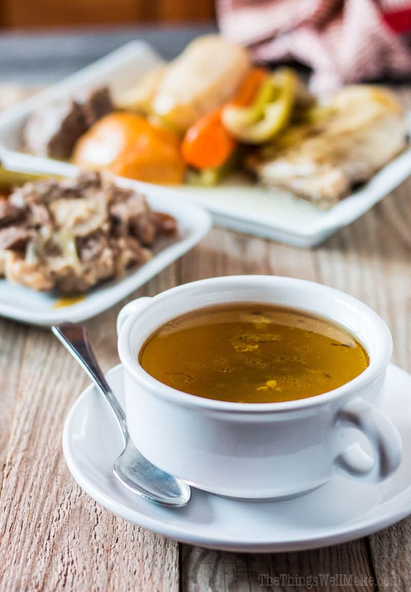 A bowl of broth in front of plates of meat and veggies