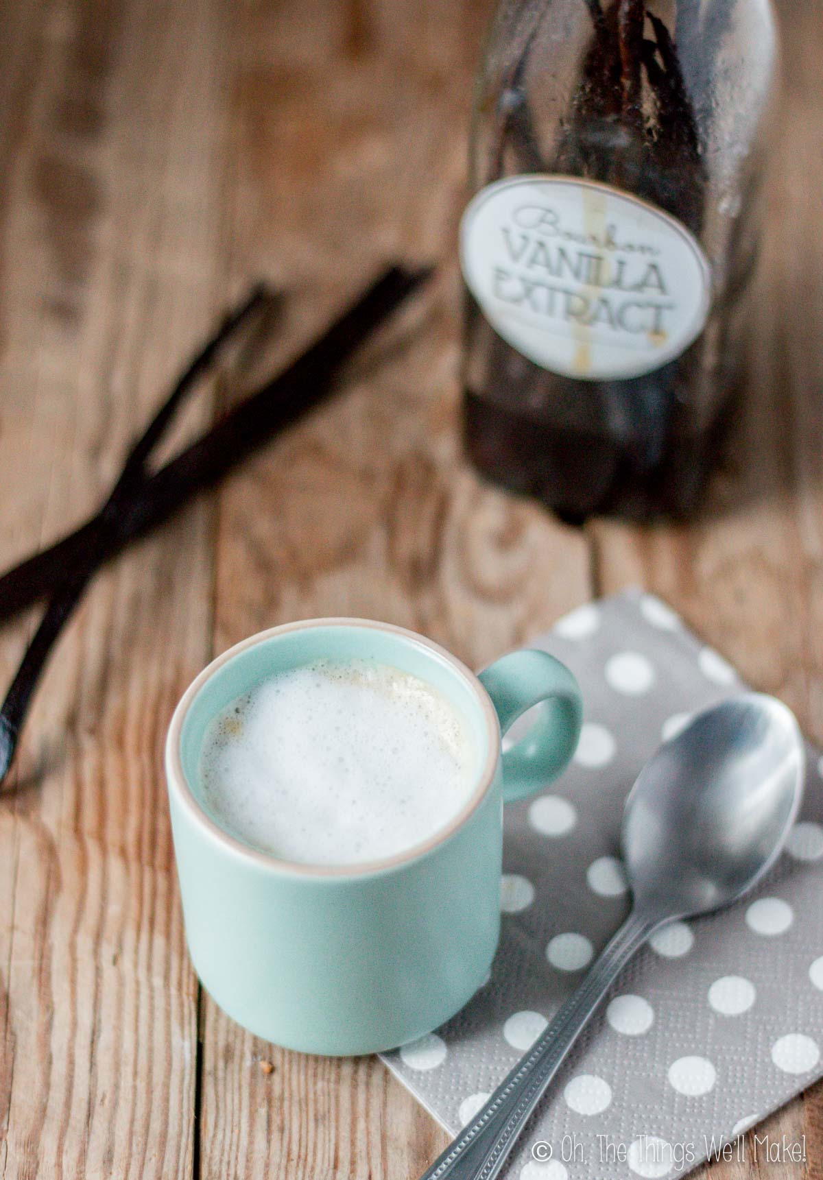 A cup of coffee with milk in front of a bottle of vanilla extract and some vanilla beans