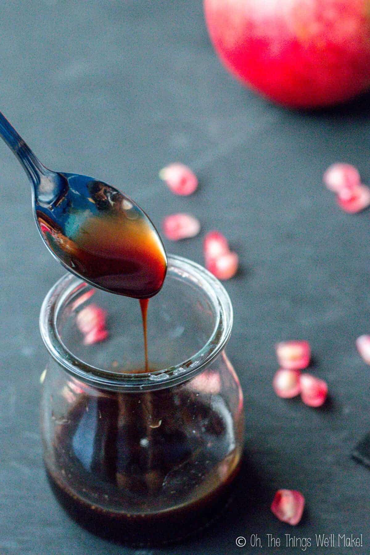 Homemade grenadine being spooned up and drizzled down into a small glass jar below.