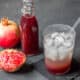 A closeup of a glass of soda and grenadine over ice in front of pomegranates and a bottle of homemade grenadine.