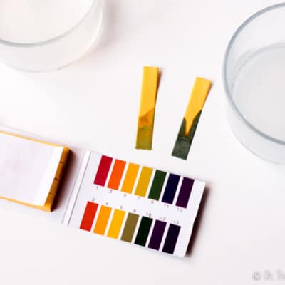 Closeup view of two pH test strips, one with a reading of around 9-10 and another at a pH 8-9.