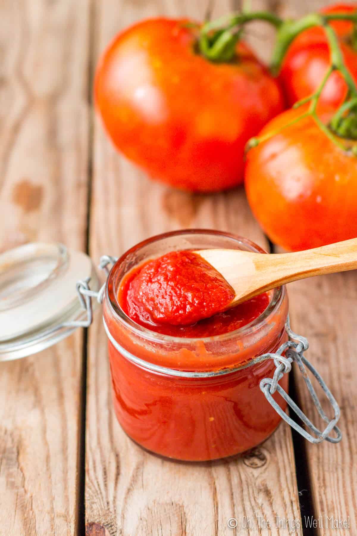 A jar of homemade tomato paste with a spoon in it, showing the texture of the tomato paste.