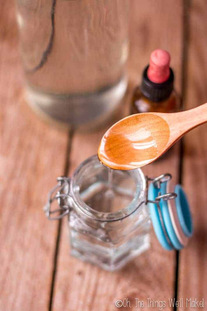 Vegerable glycerin in a jar next to a bottle of white vinegar and a bottle of essential oils.