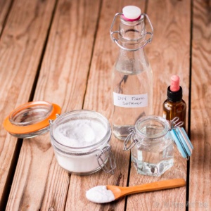 Various natural fabric softeners together in jars and bottles: baking soda, glycerin, white vinegar, and an essential oil.