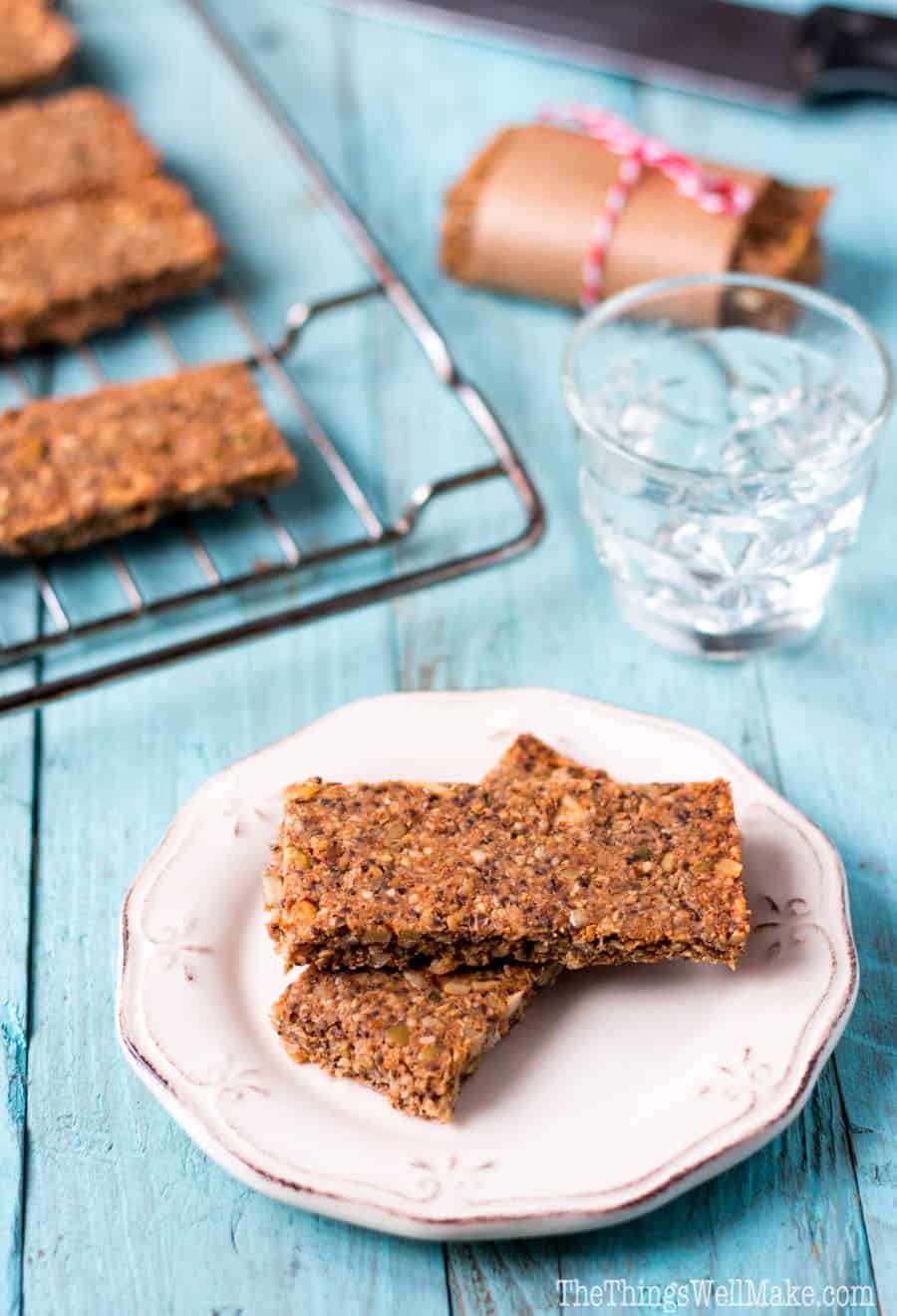 Homemade paleo granola bars on a plate in front of others on a cooling rack.