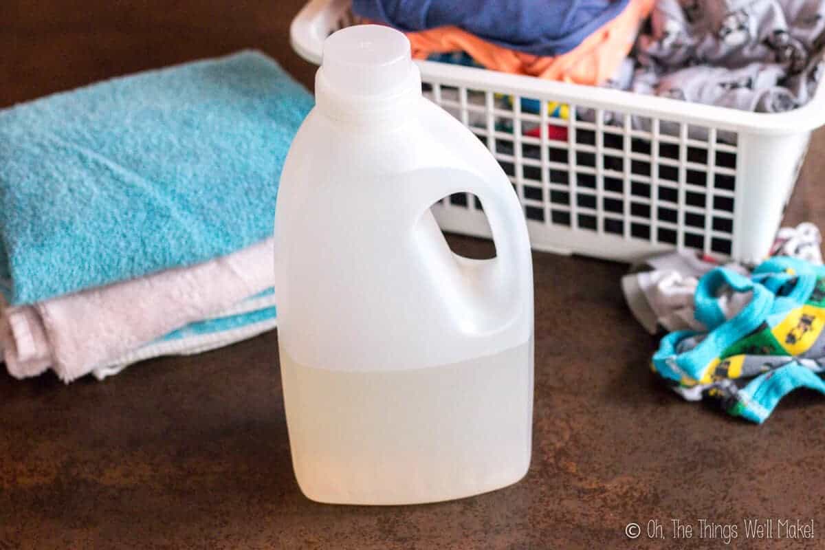 A bottle of homemade laundry detergent in front of a load of laundry.