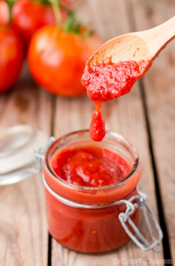 A drop fo tomato paste falling from a wooden spoon into a glass jar below