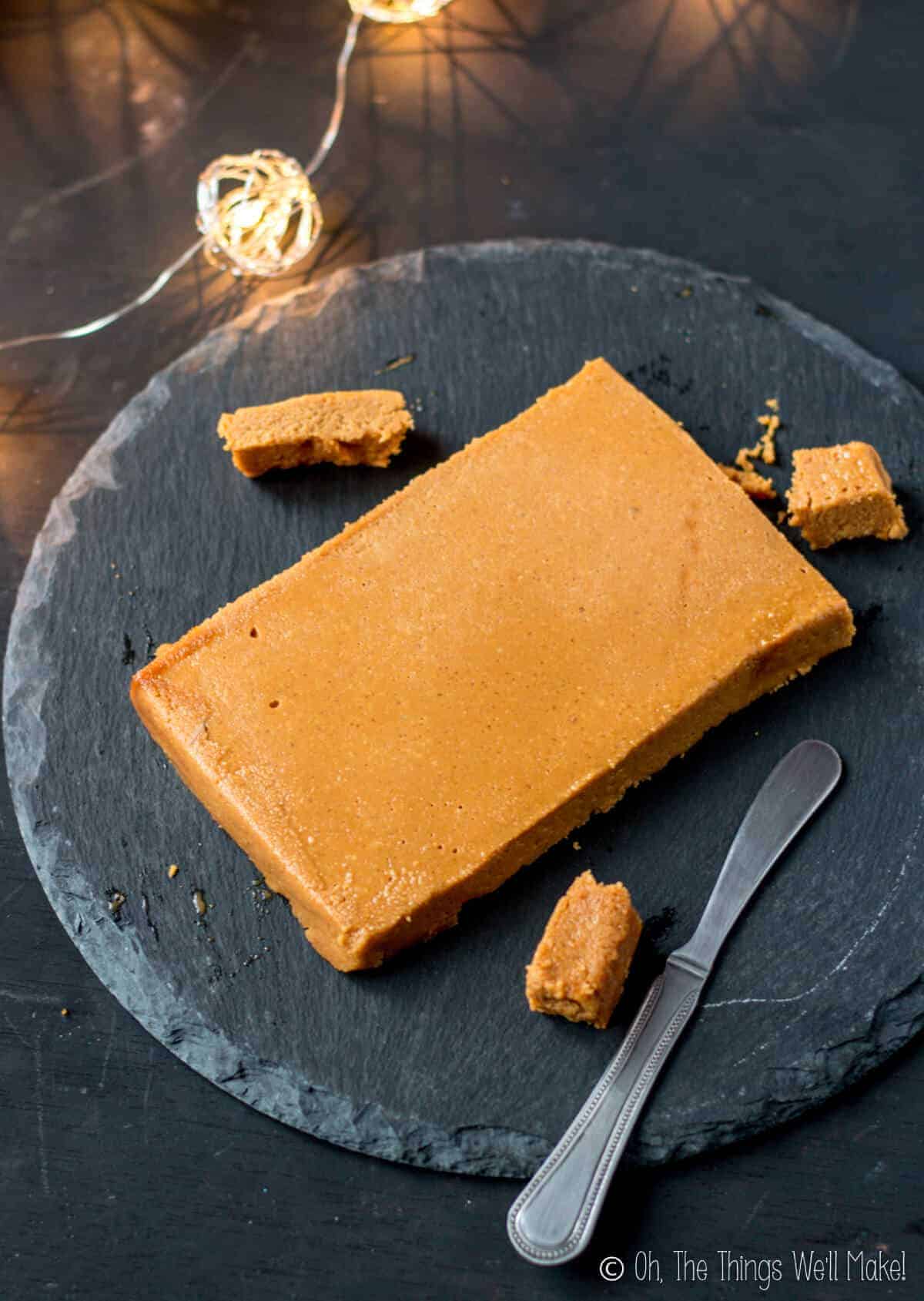 Homemade turrón de Jijona (soft almond nougat) on a round black slate platter with 3 pieces cut from it.