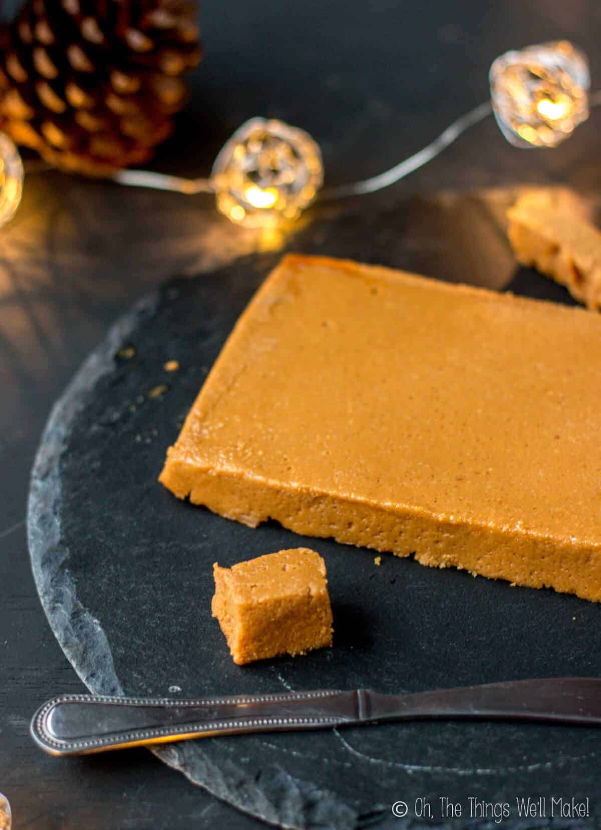 Homemade turrón de Jijona (soft almond noughat) being cut on a black slate platter in front of Christmas lights.