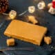 Homemade turrón de Jijona (soft almond nougat) on a black slate platter with small pieces cut from it.