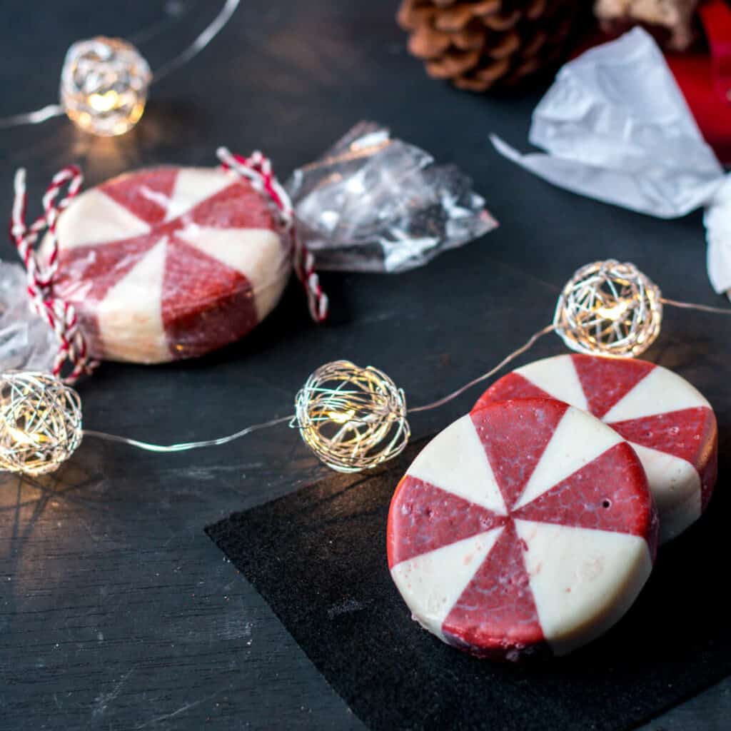 Round peppermint soaps that look like peppermint candies on a black background with Christmas lights.
