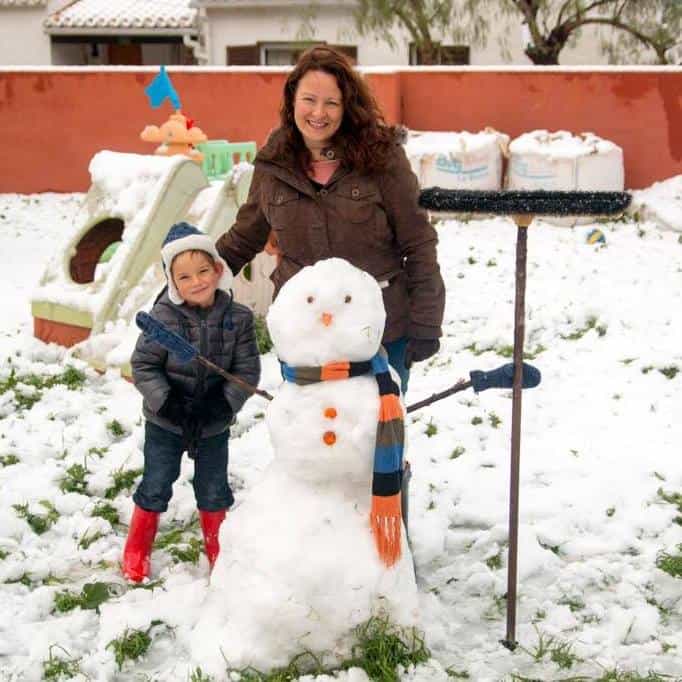 A boy and his mother standing behind a snowman