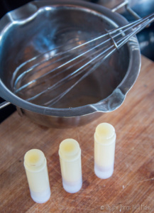 3 lip balm tubes filled with a homemade lip balm in front of a double boiler insert.