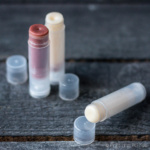 3 tubes of a homemade lip balm (2 clear and one red) with a closeup of one on its side