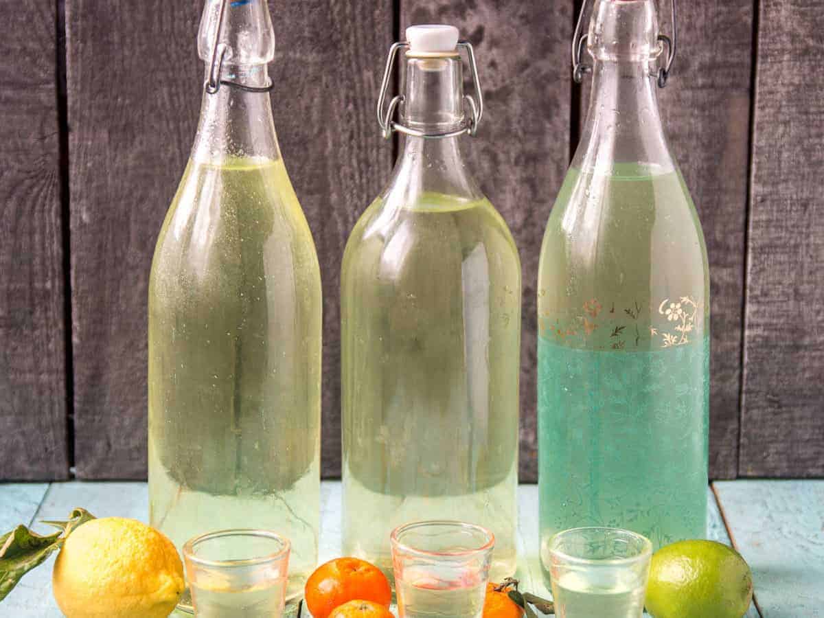 A bottle of homemade limoncello next to a bottle of homemade limecello and next to a bottle of mandarinecello