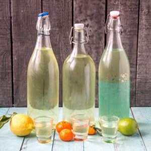 A bottle of homemade limoncello next to a bottle of homemade limecello and next to a bottle of mandarinecello