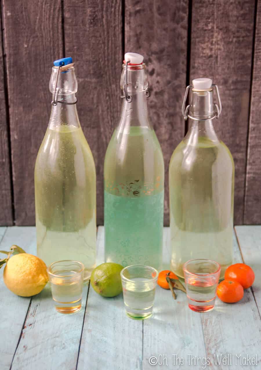 A bottle of homemade limoncello next to a bottle of homemade limecello and next to a bottle of mandarinecello