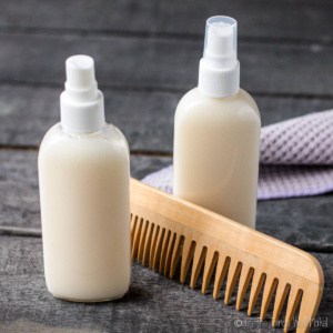 Two bottles of a homemade conditioner next to a wooden comb and a washcloth.