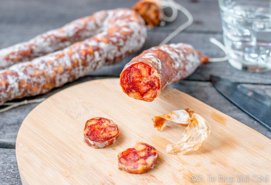 Homemade chorizo that has further dried, being sliced on a cutting board.