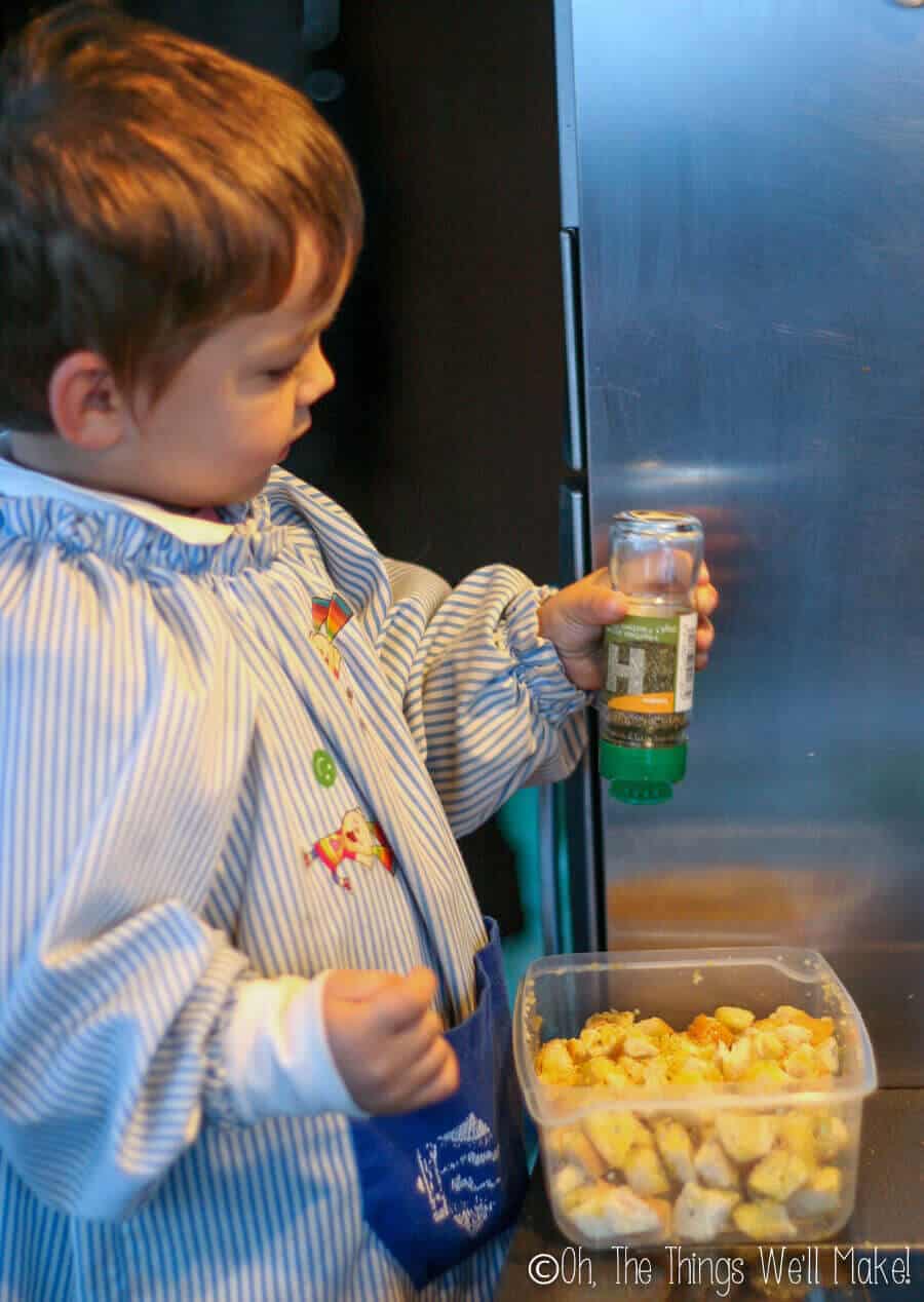 A little boy seasoning cubes of bread to make croutons