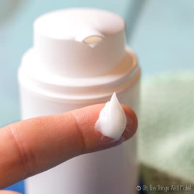 A dab of homemade moisturizer on a fingertip in front of an airless pump bottle