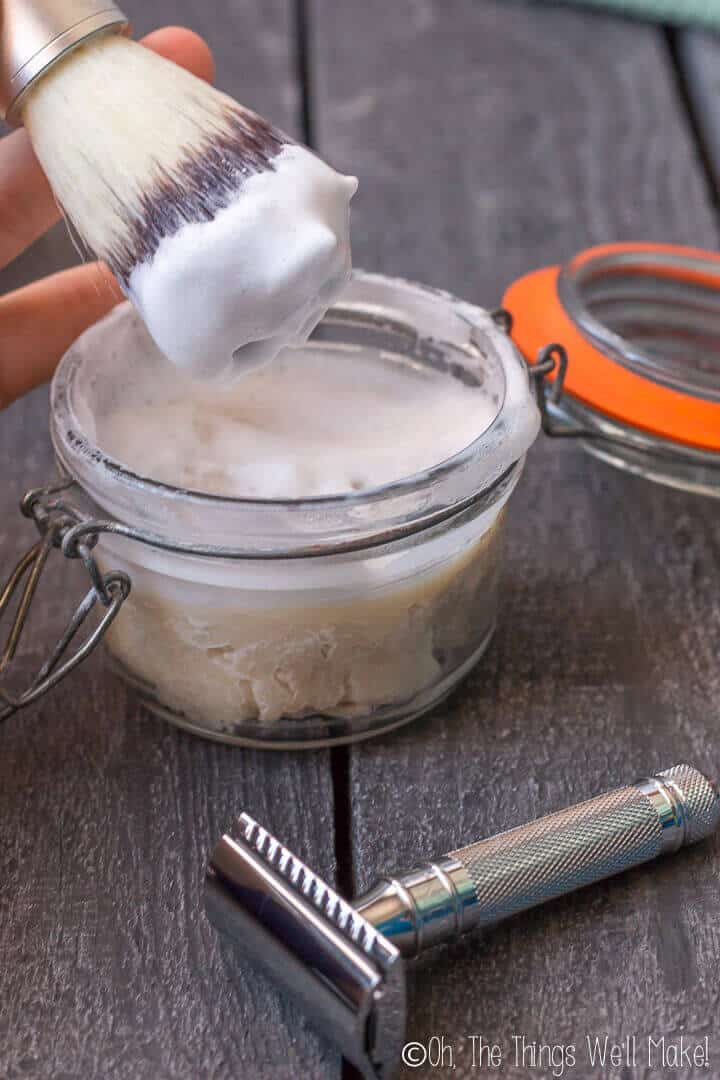 Closeup of a jar of shave soap being worked into a lather. A safety razor is in front of the jar.