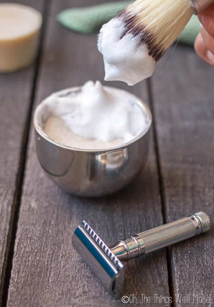 Closeup of a safety razor and lather being built up on a shave soap using a shaving brush.