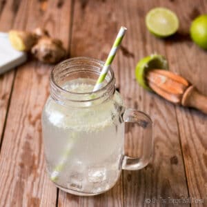Homemade ginger ale with ice in a mason jar mug in front of some ginger and lime
