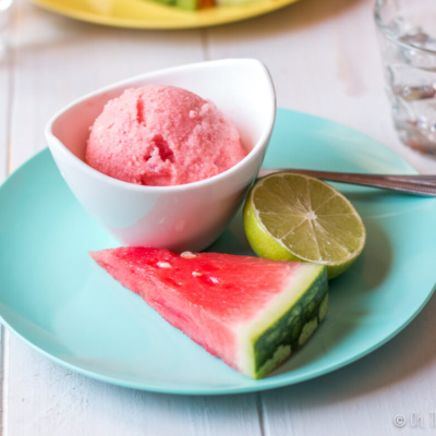 A bowl of watermelon ice cream garnished with a watermelon slice and half a lime