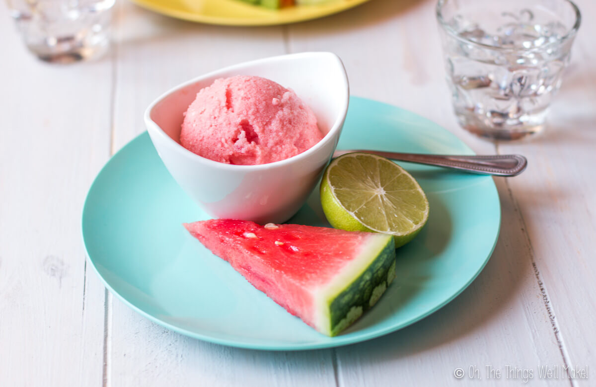 A bowl of watermelon ice cream garnished with a watermelon slice and half a lime