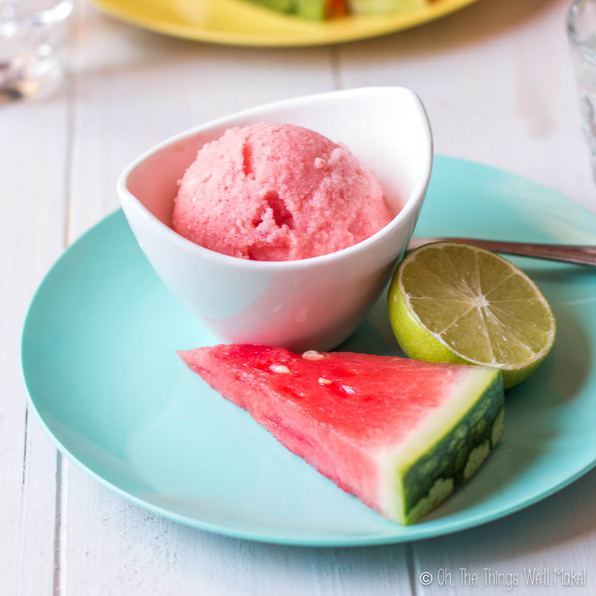 A bowl of watermelon ice cream garnished with a watermelon slice and half a lime