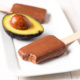 Two chocolate avocado pudding pops on a plate with half an avocado between them