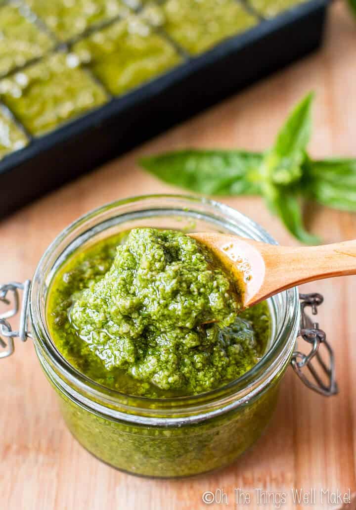 A jar of pesto sauce in front of an ice cube tray filled with more homemade pesto sauce.