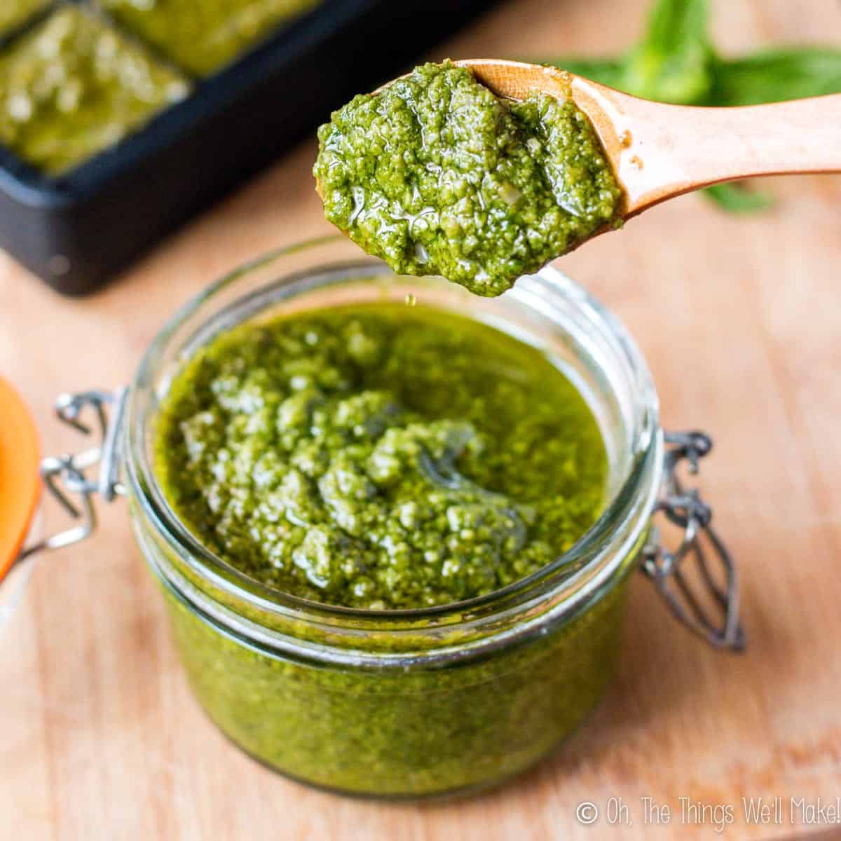 Spooning up some homemade pesto sauce out from a glass jar. 