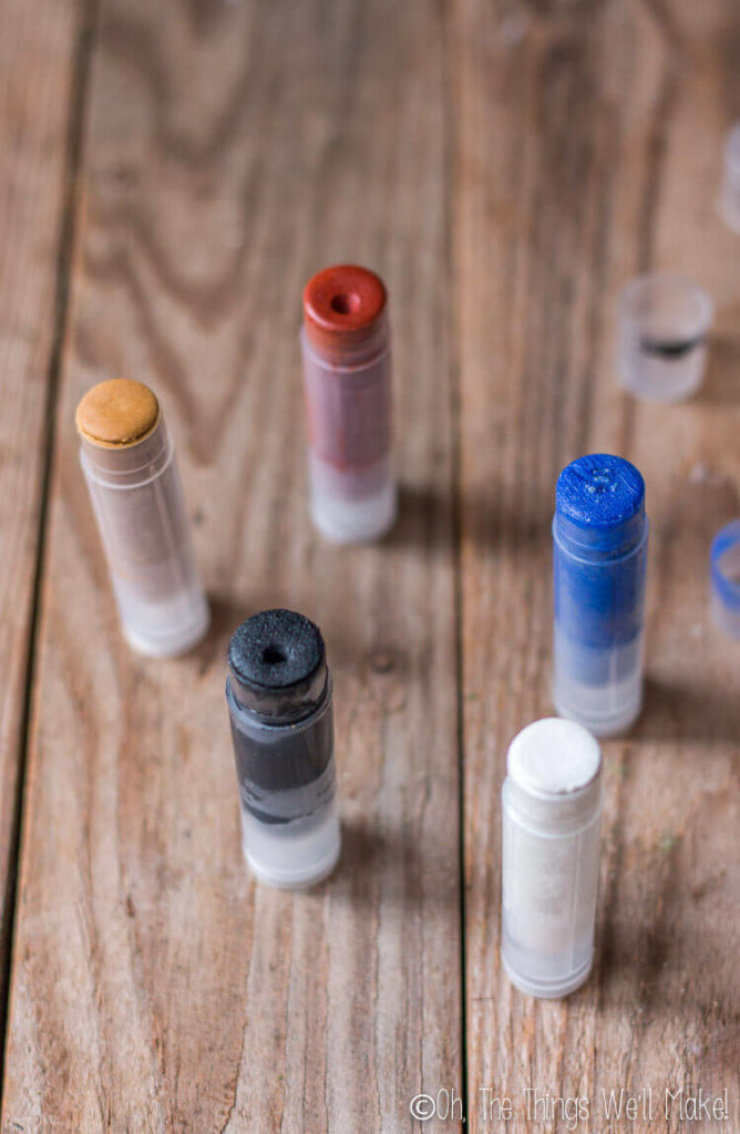 Displaying black, white, red, blue, and gold colored homemade makeup sticks in chapstick containers.